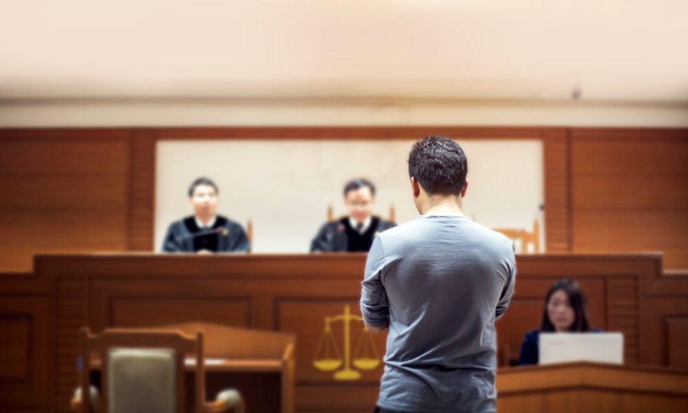 A man facing a panel of judges in a courtroom.