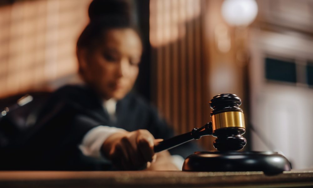 A judge holding a gavel to the face of her desk.