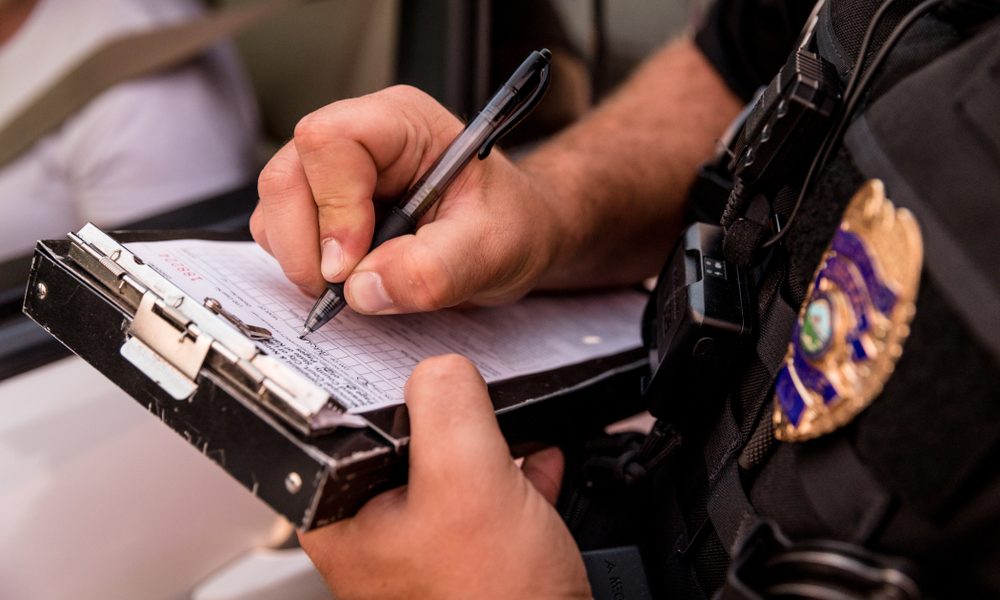 A police officer writing a traffic ticket while standing outside of a parked vehicle.