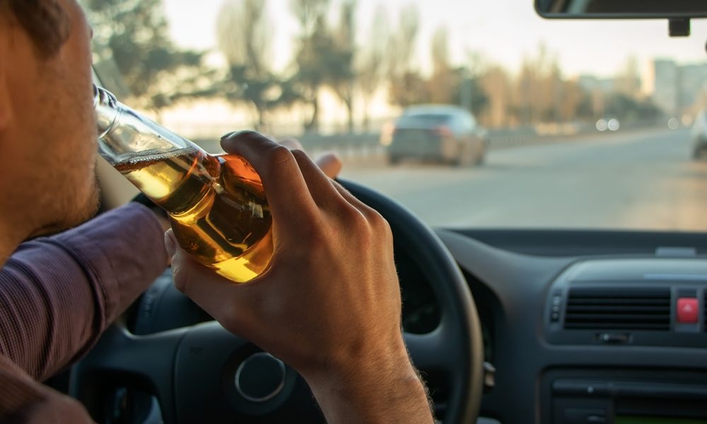 View from the backseat of a moving vehicle while the driver takes a drink of beer.