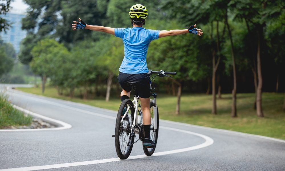 A woman riding a bicycle on a road, her hands outstretched.