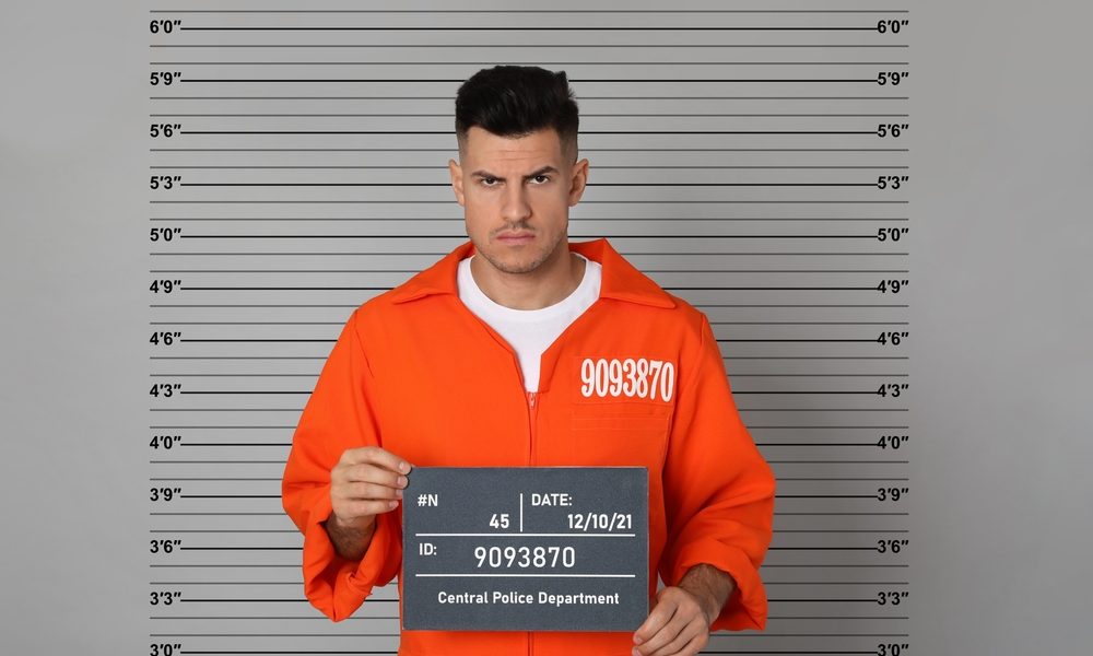 A man in an orange jumpsuit taking a mugshot.