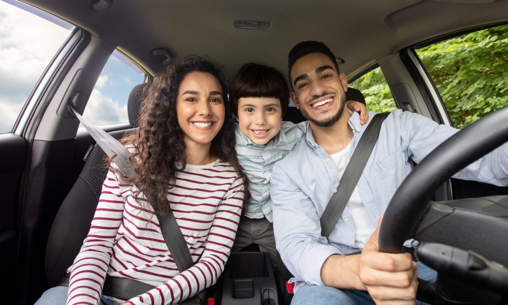 A mother, father, and child smiling while inside of a vehicle.