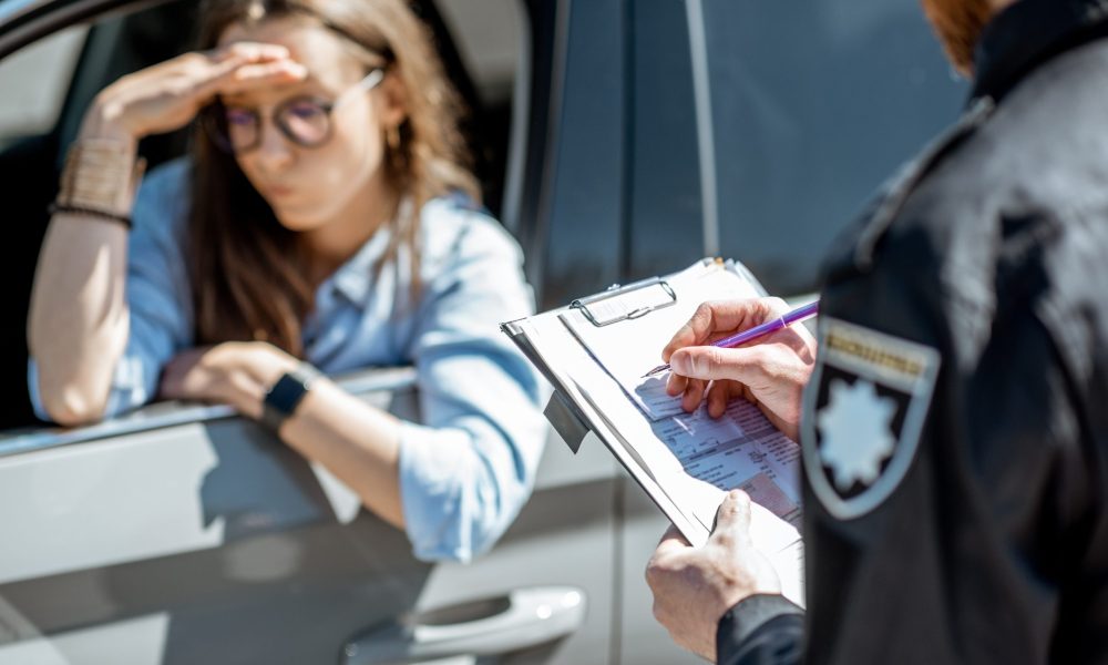 A police officer writing at icket while the driver holds her head in her hands.